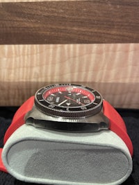 a watch with a red strap sitting on top of a wooden box