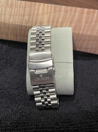 a stainless steel watch bracelet sitting on a piece of wood