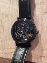 a watch with a black leather strap sitting on a wooden table