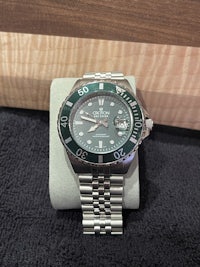 a watch with a green dial sitting on top of a box