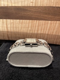 a silver watch sitting on a wooden cutting board