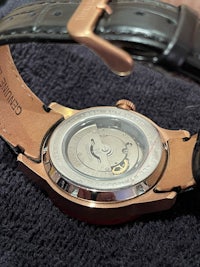 a watch with a black leather strap and a rose gold dial