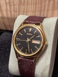 a gold watch with a brown strap sitting in a box