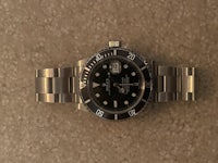 a black rolex submariner watch on a carpet