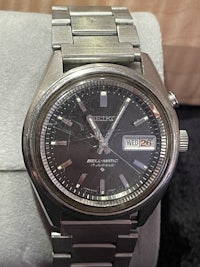 a silver watch with a black dial sitting on top of a box