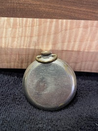 a small pocket watch sitting on top of a piece of wood