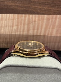 a gold watch with a burgundy strap sitting on a table