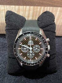 an omega speedmaster watch sitting on a pillow